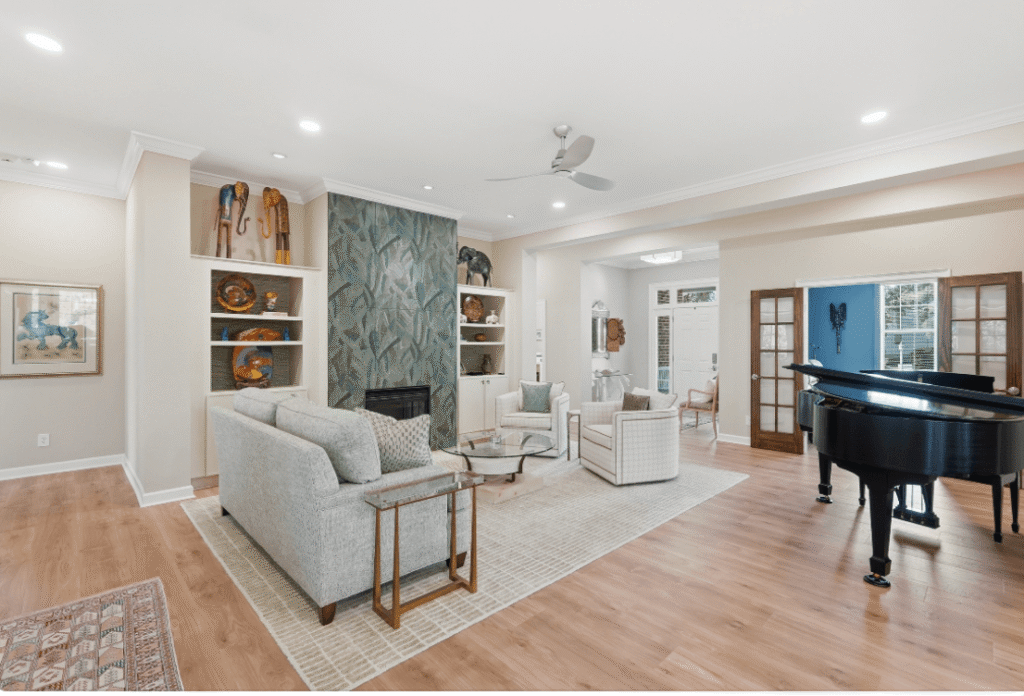 Modern living room with neutral furniture, fireplace, built-in shelves, a black grand piano, wood flooring, and large windows providing natural light.