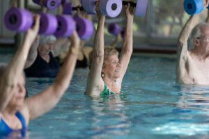 Senior ladies at a water aerobics class lift weights above their heads