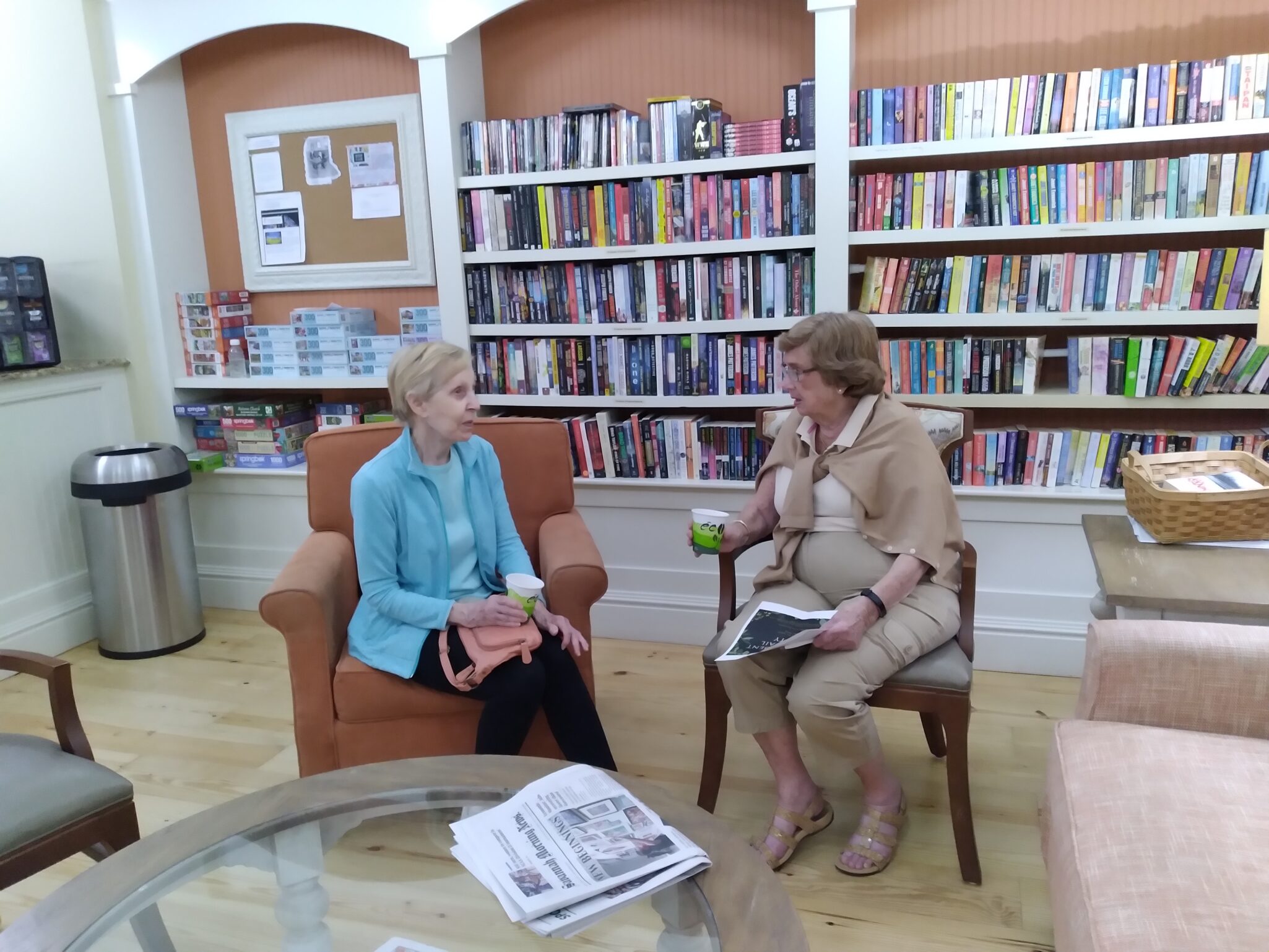 Two women sitting in chairs in front of a bookcase.