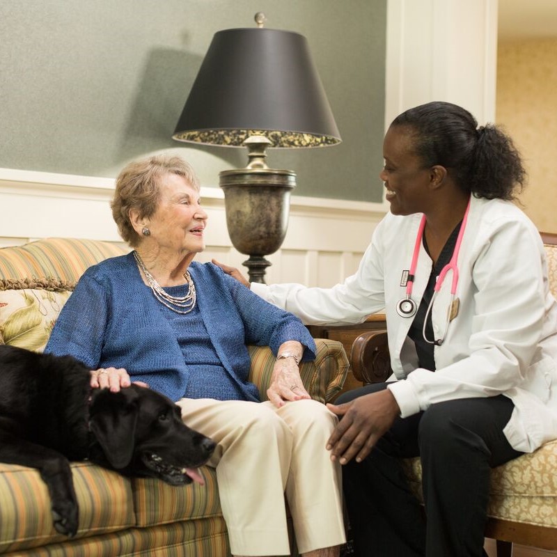 A nurse talking to an elderly woman and her dog.