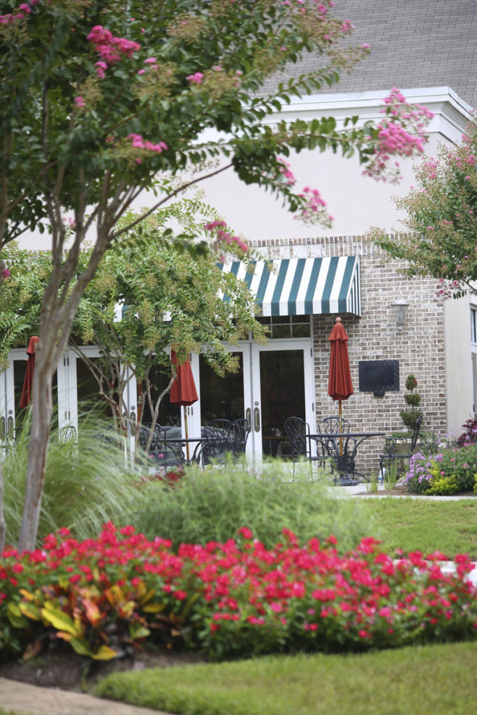 An exterior photo of manicured lawns and gardens and an outdoor seating patio for a restaurant