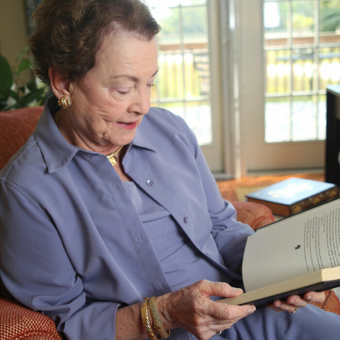 An elderly woman sits in an armchair and reads a book