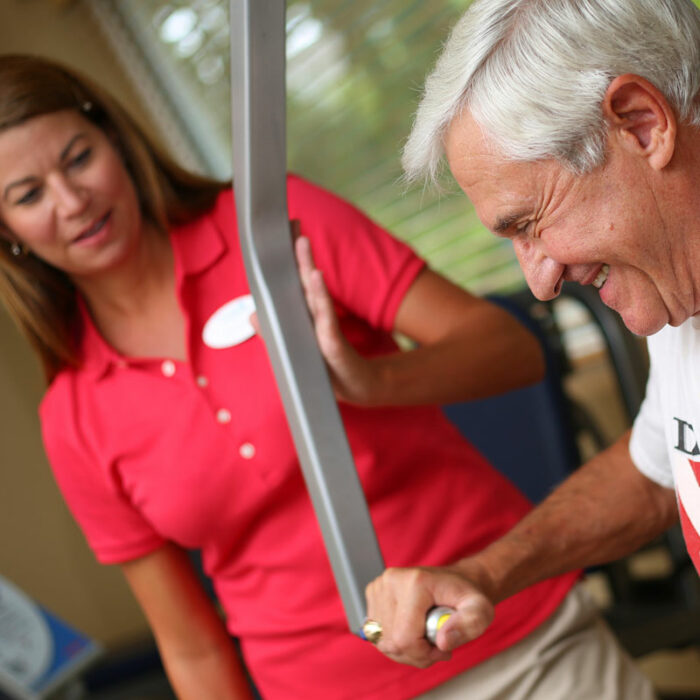 A trainer helps a senior man use workout machines