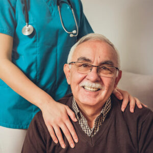Senior gentleman smiling with caregivers hands on his shoulders