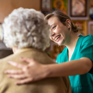 Caregiver smiling at an elderly woman with a hand on her back.